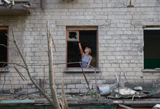 A woman removes a broken glass in a damaged apartment building after the shelling in Donetsk, Russian-controlled Ukraine